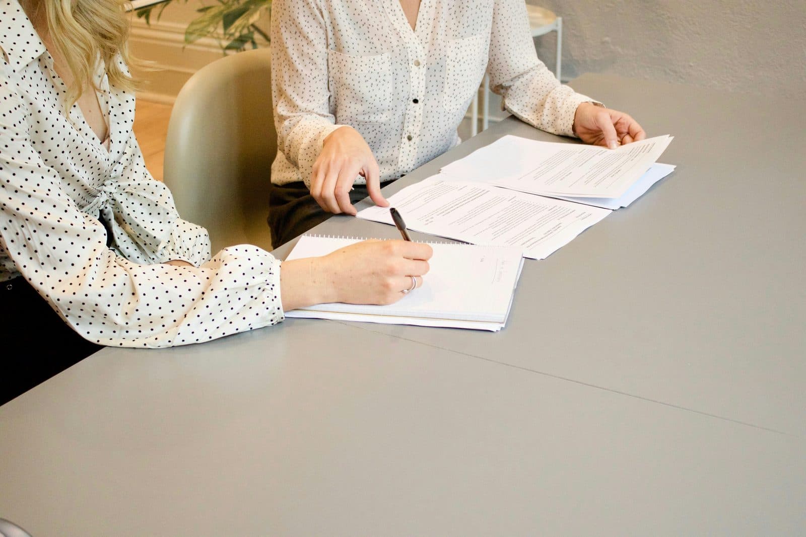 Two people reading printed papers at a table, one holding a pen