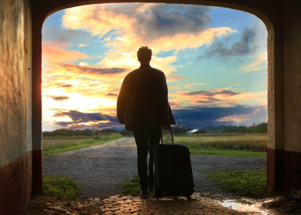 A man with a suitcase walking out toward a sunrise