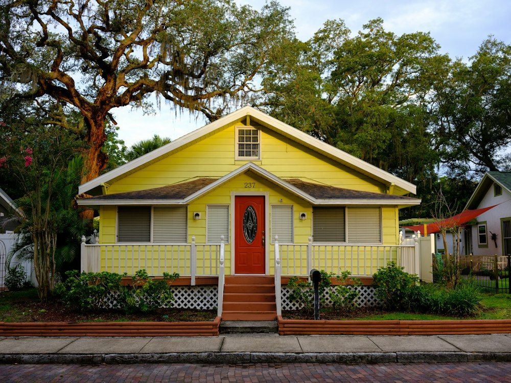 A yellow family home with a front porch under old oak trees